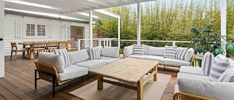 A covered outdoor seating area with a wooden table, sofas, and chairs.