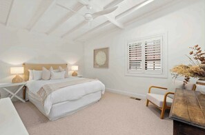 A bedroom with a large bed, bedside tables with lamps, a window with blinds, a wall art piece, and a wooden table with a vase of dried flowers. - Conifer - Pet Friendly with Outdoor Spa (Callala Beach)