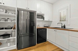A modern kitchen with white cabinets, a stainless steel refrigerator, a microwave, and a sink. - Conifer - Pet Friendly with Outdoor Spa (Callala Beach)