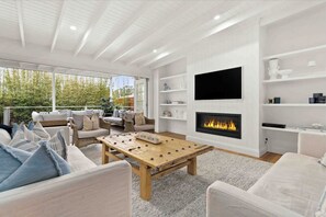 A modern living room with a fireplace, white walls, and a large window overlooking greenery. - Conifer - Pet Friendly with Outdoor Spa (Callala Beach)