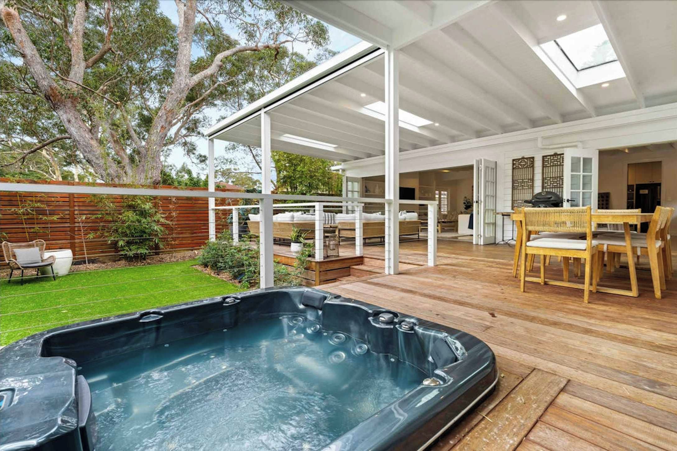 Een modern terras buiten met een jacuzzi, houten vloer en een overdekte zithoek.