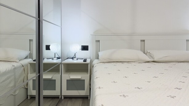 A hotel room with a mirrored wardrobe, a bedside table with a lamp, and a bed with a floral-patterned duvet. - Casa Nina Seconda - Sanremo (Sanremo)