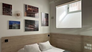 A bedroom with a bed, white bedding, a gray throw, and four framed pictures on the wall.