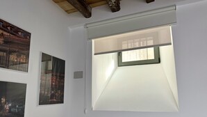 A room with a large window, wooden beams on the ceiling, and three framed pictures on the wall.