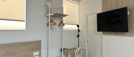 Una habitación moderna con cama, escritorio, silla, televisor y armario con perchas de madera.
