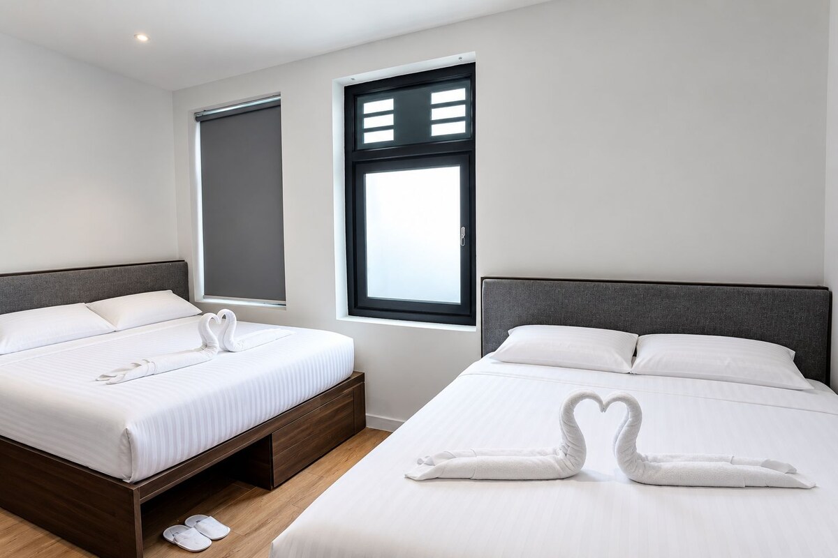Une chambre d’hôtel avec deux lits, chacun doté d’une tête de lit, et une fenêtre avec des stores.