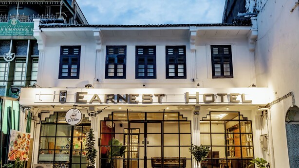 The Ernest Hotel facade with large windows, a signboard, and potted plants. - Earnest Hotel Georgetown (George Town)