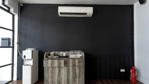 A room with a water dispenser, a small wooden cabinet, a black wall, a fire extinguisher, and a window. - Earnest Hotel Georgetown (George Town)