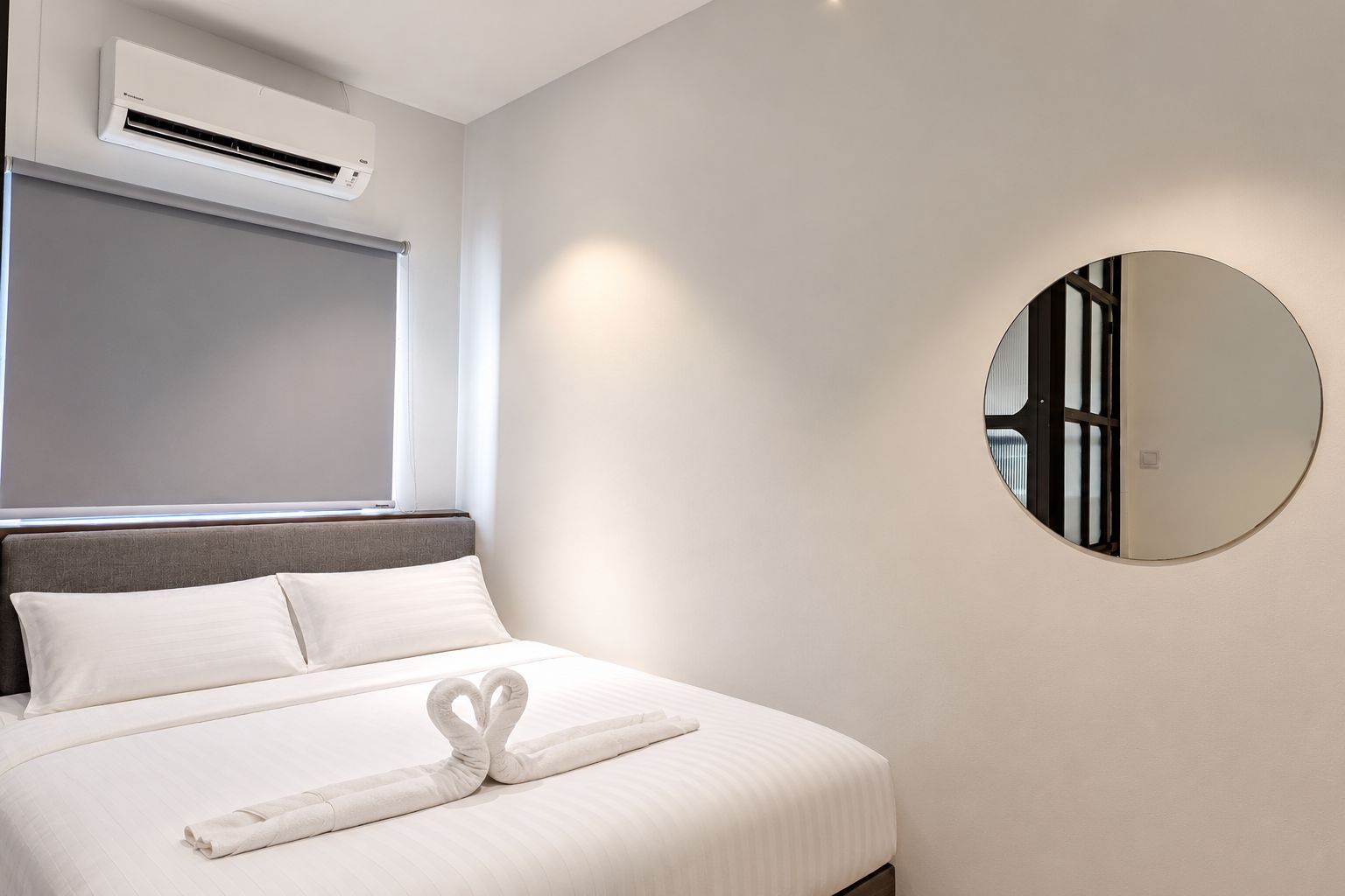 A hotel room with a bed, a round mirror, and an air conditioning unit.