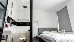A modern hotel room with a shower, sink, toilet, and a bed with towels. - Earnest Hotel Georgetown (George Town)