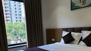 A hotel room with a large bed, a wooden headboard, a window with curtains, and a painting on the wall. - Innzoy Hotels - DLF Road (Hyderabad)