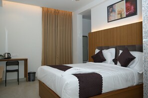 A hotel room with a bed, a desk, a chair, and a trash bin. - Innzoy Hotels - DLF Road (Hyderabad)