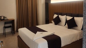 A hotel room with a large bed, a desk, a chair, a ceiling fan, and a painting on the wall. - Innzoy Hotels - DLF Road (Hyderabad)
