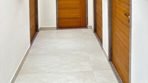 A hallway with three wooden doors, each with a metal handle, and a light fixture on the ceiling. - Innzoy Hotels - DLF Road (Hyderabad)