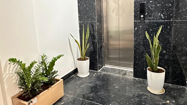 A lobby with a marble floor, two potted plants, an elevator, and a white wall. - Innzoy Hotels - DLF Road (Hyderabad)