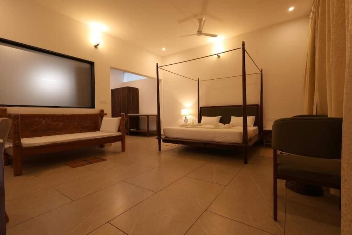 A room with a four-poster bed, a sofa, a chair, a television, and a ceiling fan.