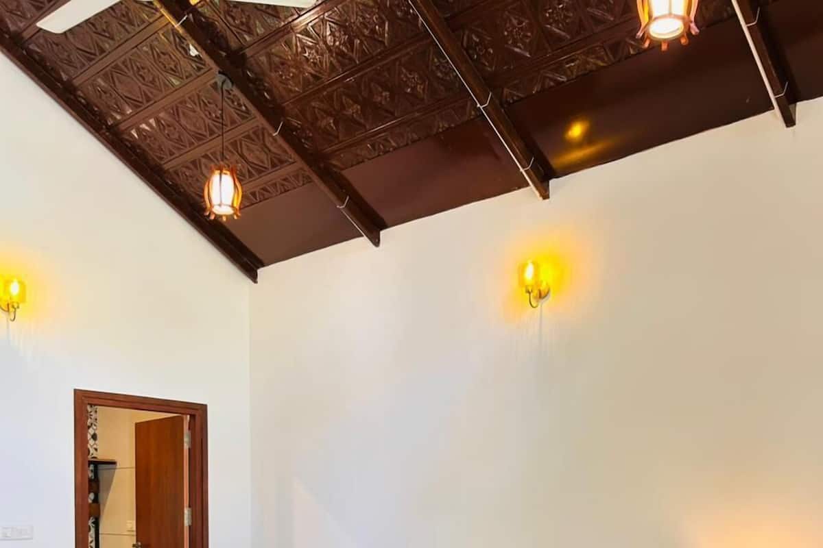 A bedroom with a wooden bed, two bedside tables, a nightstand, a chair, a small table, and a ceiling with decorative woodwork.