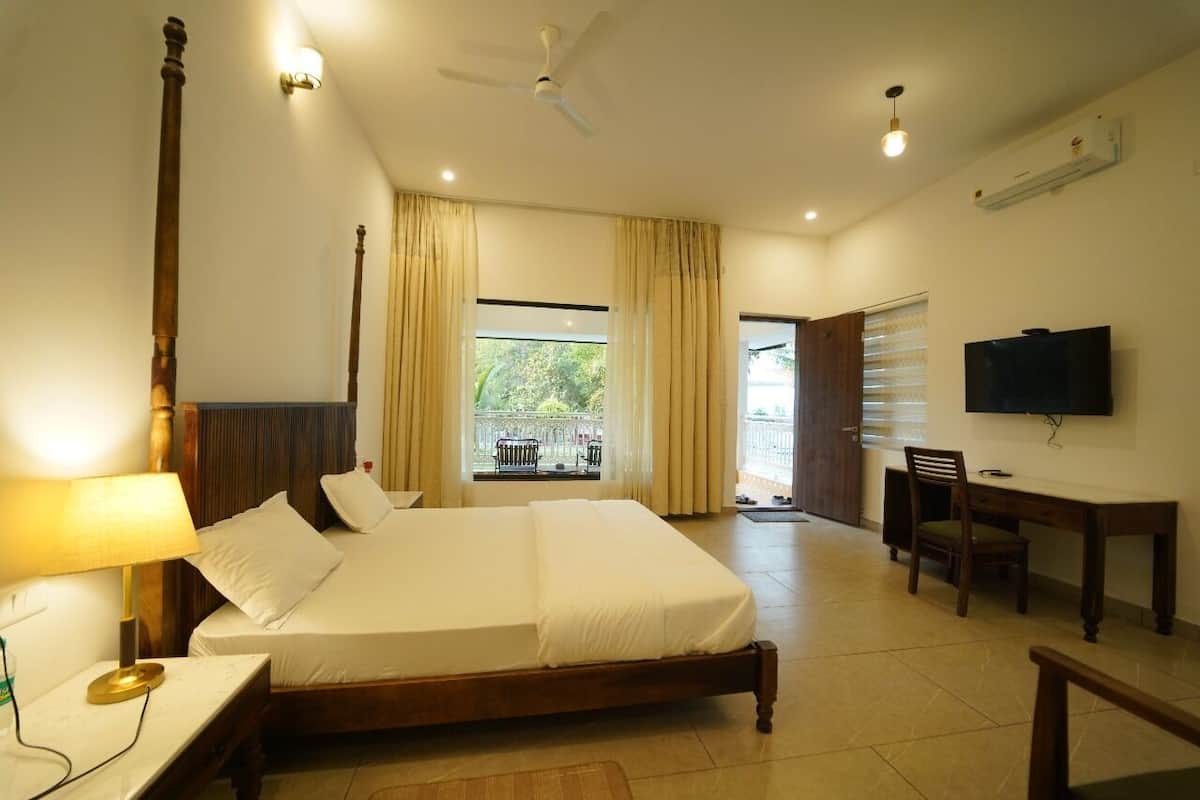 A bedroom with a large bed, a desk, a chair, a television, and a balcony with a view of greenery.