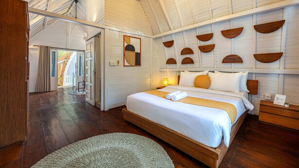 A spacious bedroom with a large bed, wooden headboard, and a sloped ceiling. - Cove Wong Village (Tumbak Bayuh)