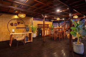 A restaurant interior with a wooden ceiling, woven wall panels, and a bar area with stools and a refrigerator. - Cove Wong Village (Tumbak Bayuh)
