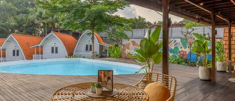 A pool area with a wooden deck, wicker furniture, and a mural on the wall.