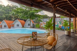 A pool area with a wooden deck, wicker furniture, and a mural on the wall. - Cove Wong Village (Tumbak Bayuh)