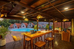 A covered outdoor area with a pool, wooden furniture, and a bar. - Cove Wong Village (Tumbak Bayuh)