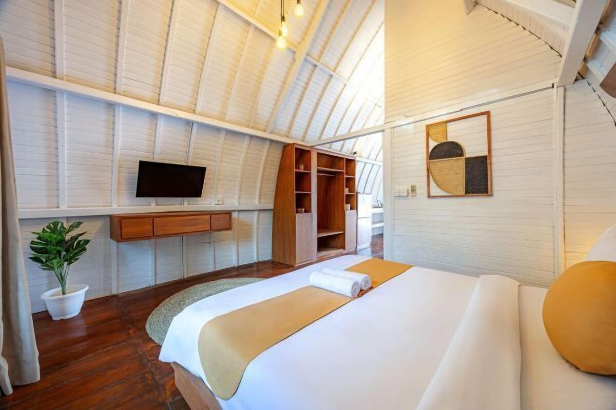 A bedroom with a large bed, a TV mounted on the wall, wooden storage, and a potted plant.
