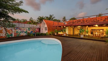 A swimming pool with a wooden deck, a colorful mural, and a building with a red roof.