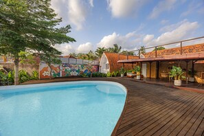 A swimming pool with a wooden deck, a colorful mural, and a covered seating area with plants. - Cove Wong Village (Tumbak Bayuh)