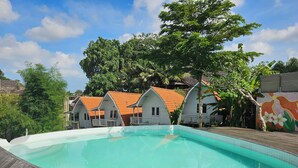 A swimming pool with a wooden deck, surrounded by white buildings with orange roofs. - Cove Wong Village (Tumbak Bayuh)