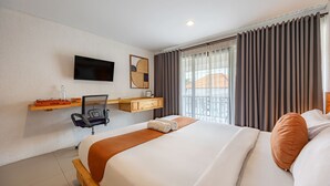 Habitación de hotel con cama, escritorio con silla, televisor montado en la pared y ventana con cortinas.
