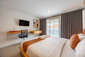 Habitación de hotel con cama, escritorio con silla, televisor montado en la pared y ventana con cortinas.