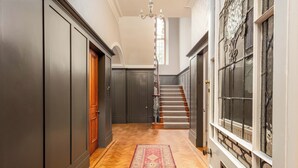 Un couloir doté d’un plancher en bois, d’un tapis rouge à motifs, d’un escalier avec une rampe en bois et d’une fenêtre décorative aux motifs complexes.