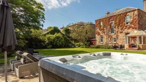 Un bain à remous dans un jardin, avec un bâtiment en pierre et une pelouse.
