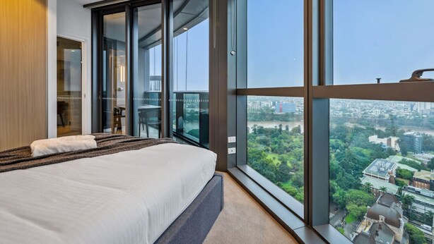 A modern bedroom with a large bed, sliding glass doors leading to a balcony, and a city view.
