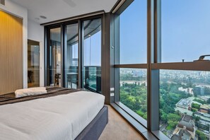 Un dormitorio moderno con una cama grande, puertas de cristal correderas que dan a un balcón y vistas a la ciudad.
