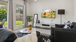 Una sala de estar moderna con un ventanal grande, una araña, un televisor de pantalla plana y un sofá con cojines estampados.