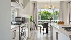 Una cocina moderna con microondas, estufa y horno integrados. Hay un comedor con mesa y sillas, y un amplio ventanal con vistas al follaje exterior.