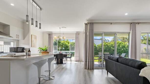 Una cocina moderna con una isla central, taburetes de bar y un comedor con vistas al exterior.