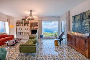 Una sala de estar con una amplia estantería, televisor y vista al mar.