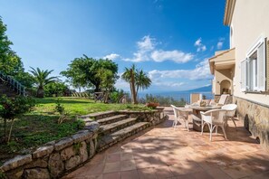 A patio with outdoor furniture, a stone wall, and a view of the sea.