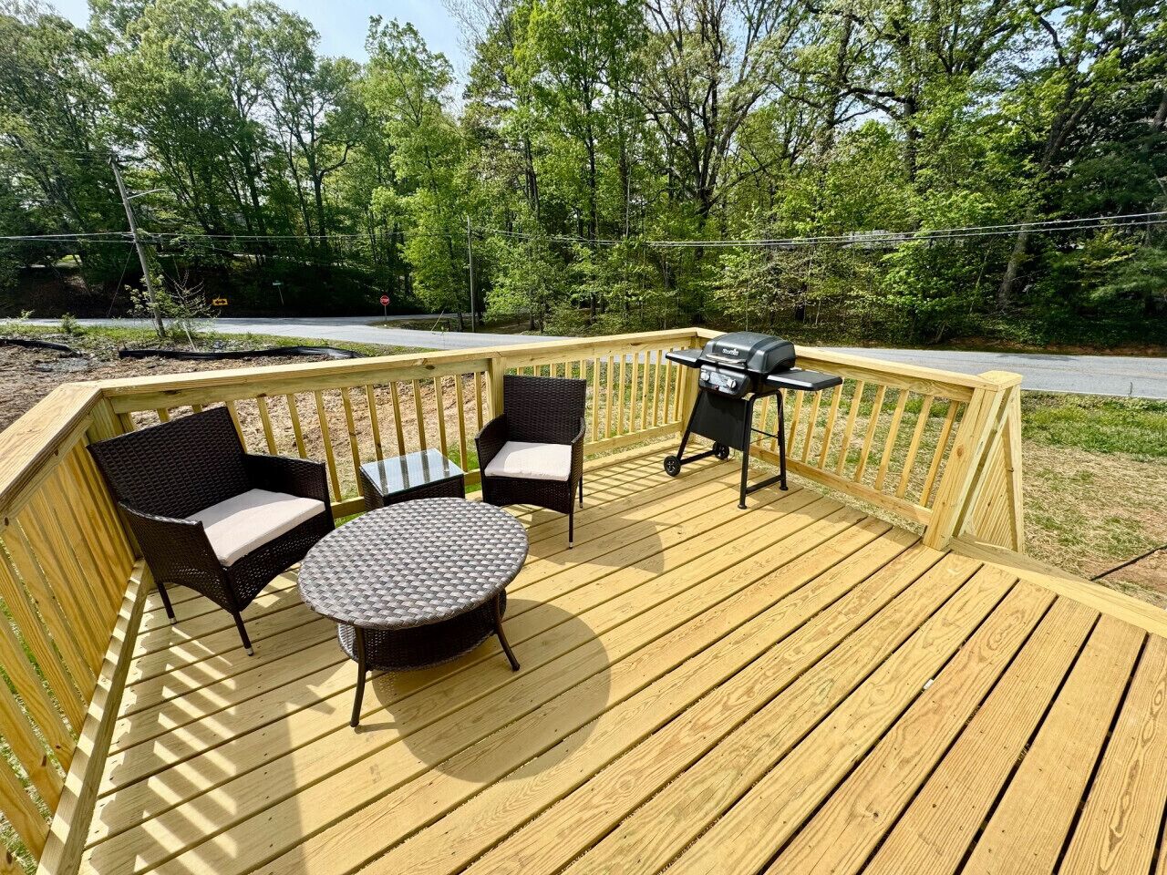 Une terrasse en bois aménagée avec du mobilier d’extérieur, notamment deux fauteuils en osier et une table ronde.
