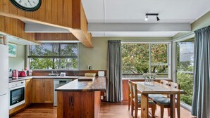 A modern kitchen with wooden cabinets, a central island, and a dining area with a table and chairs. - Richards - Spacious, charming, private and cosy, with Spa Bath and large outdoor deck (Taupō)