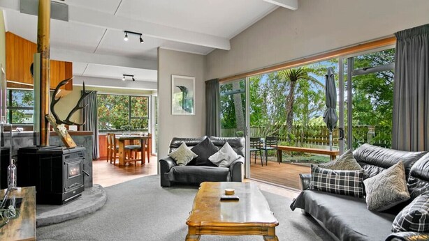 A spacious living room with a fireplace, a sofa set, and a dining area. - Richards - Spacious, charming, private and cosy, with Spa Bath and large outdoor deck (Taupō)