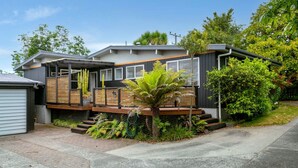 A modern two-story house with a wooden deck, large windows, and a small garden area with a palm tree. - Richards - Spacious, charming, private and cosy, with Spa Bath and large outdoor deck (Taupō)