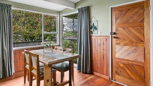A dining area with a wooden table and chairs, large windows with curtains, and a wooden door. - Richards - Spacious, charming, private and cosy, with Spa Bath and large outdoor deck (Taupō)