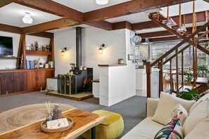 Una sala de estar acogedora con chimenea, vigas de madera y una escalera que sube a un nivel superior.