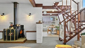 A cozy living room with a fireplace, wooden staircase, and a dining area.