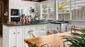 A modern kitchen with white cabinetry, a wooden dining table, and a view of a garden through large windows.